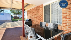 An outdoor patio with a glass table and chairs, a grill, and a brick wall. - Kingfisher - Pet-Friendly - 10 Min Walk to Beach (Sanctuary Point)