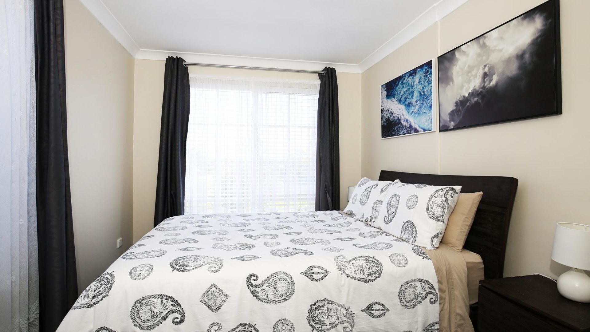 Habitación de hotel con una cama, una mesita de noche, una lámpara y dos cuadros en la pared.