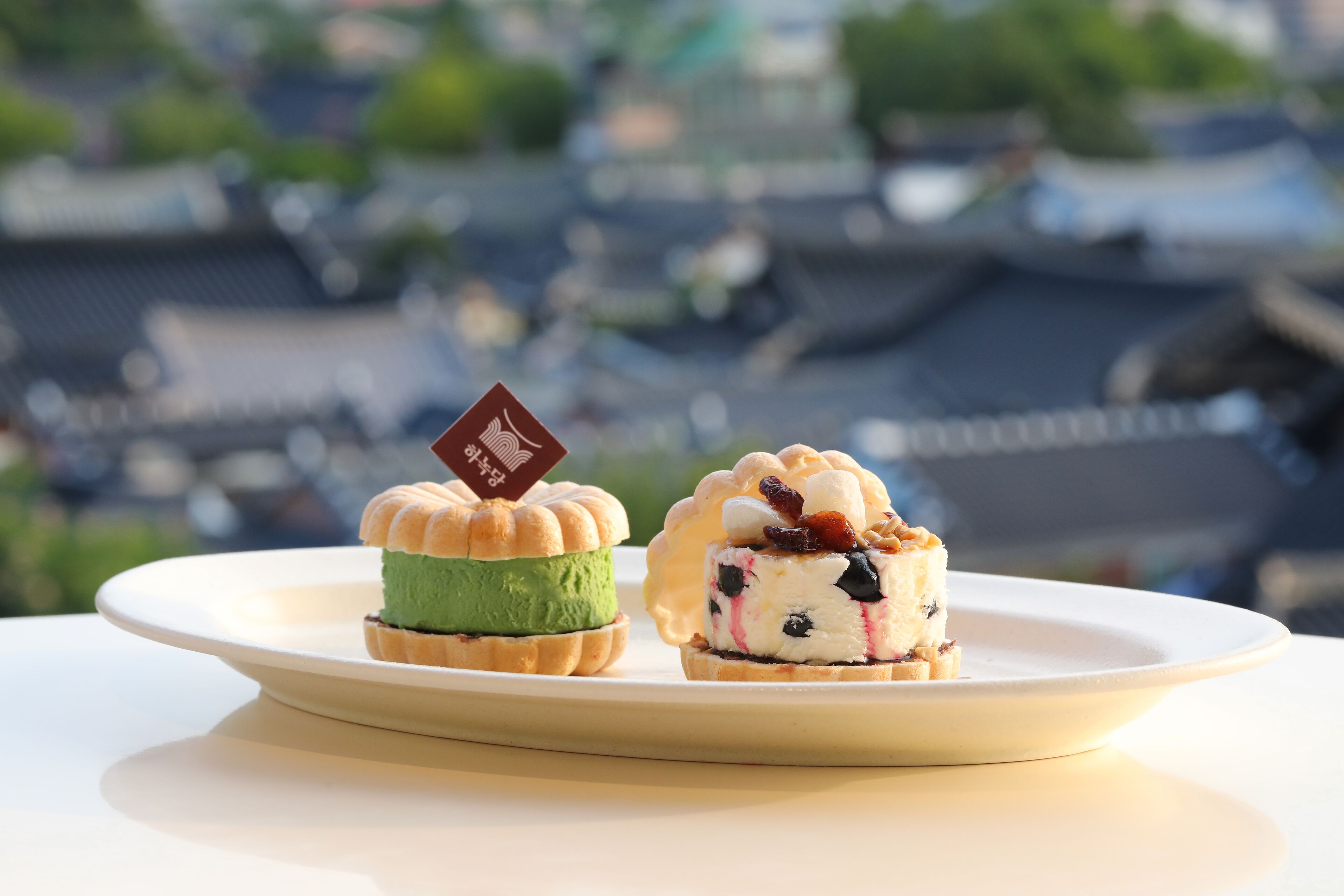 Two desserts on a plate with a cityscape in the background.
