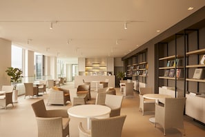 Un área de estar moderna con mobiliario de mimbre, una mesa de centro y una estantería llena de libros.