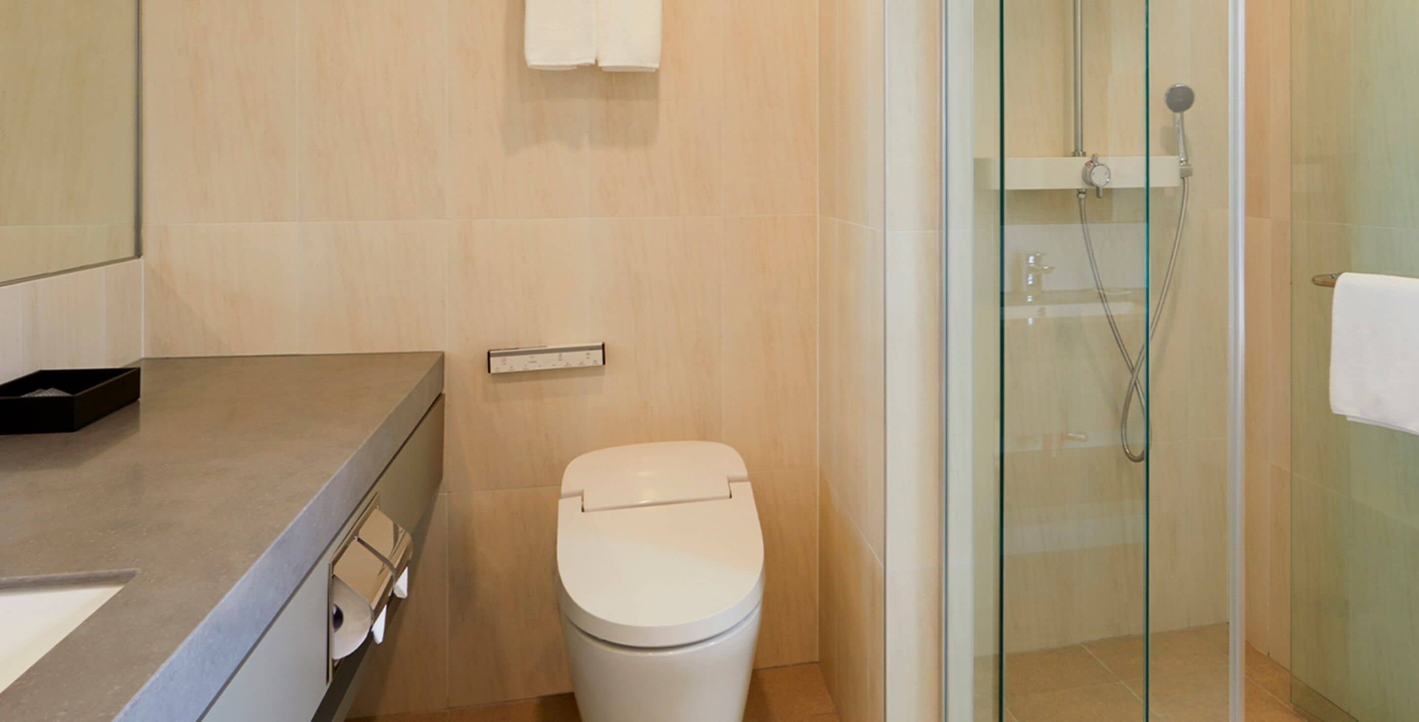 Een badkamer met een toilet, een douchecabine van glas en een beige betegelde muur.