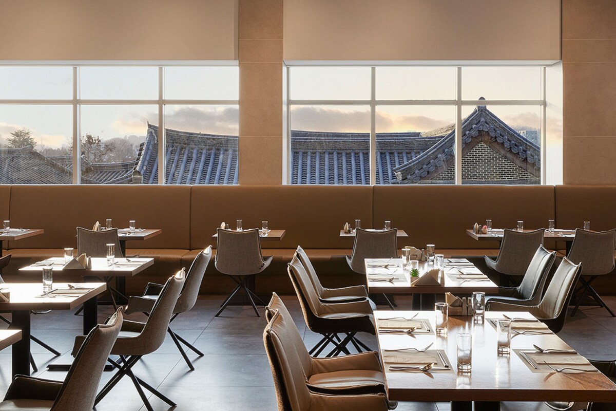 A restaurant with tables and chairs arranged in rows, large windows with a view of traditional architecture, and a modern interior design.