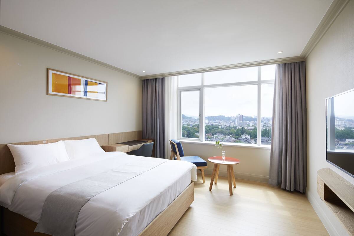 Une chambre d’hôtel avec un grand lit, un bureau, une chaise, une petite table et un téléviseur.
