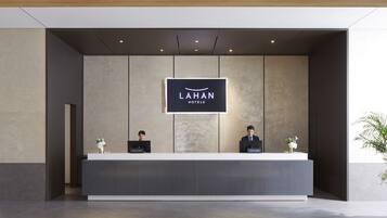 A reception desk with a sign reading "LAHAN HOTELS" and two receptionists.