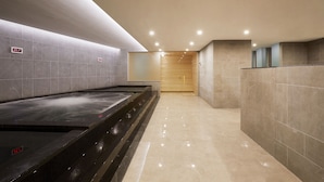 Een modern wellnessgedeelte met een verwarmde vloer, een houten sauna en een betegelde muur met een digitale klok.