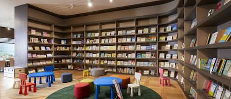 A children's library with bookshelves, colorful chairs, a small fire truck model, and a round table.