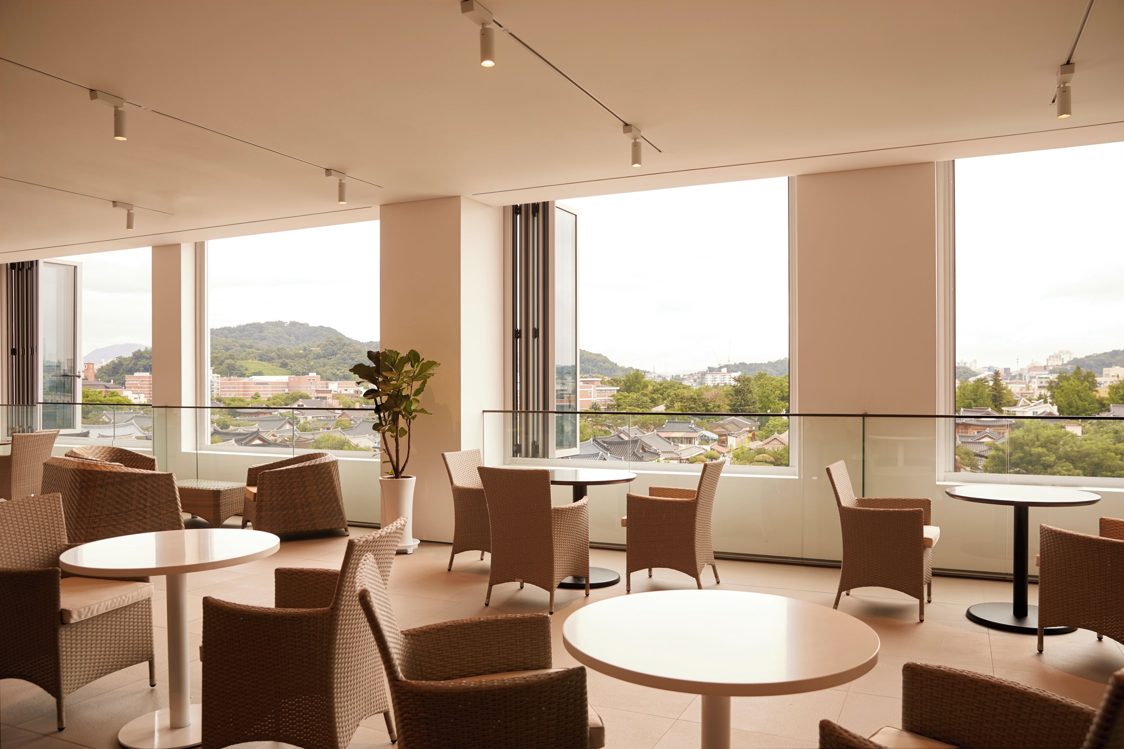 Une chambre d’hôtel moderne avec de grandes fenêtres, des meubles en osier et une vue sur le paysage urbain.