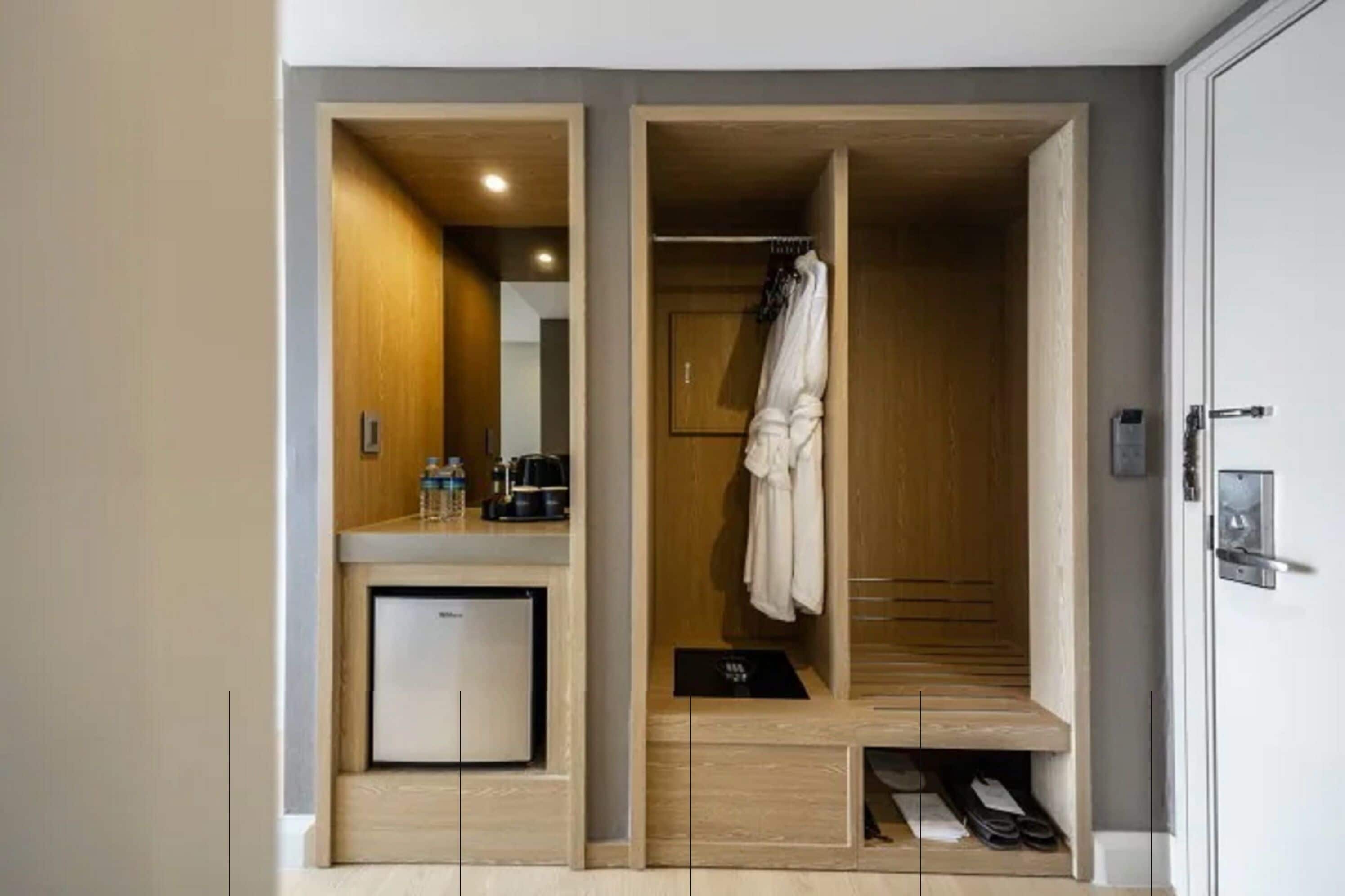 Une chambre d’hôtel avec une armoire en bois, un petit minibar et un porte-chaussures.