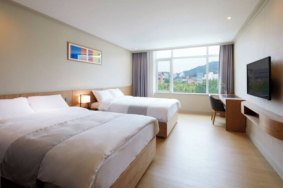 Une chambre d’hôtel avec deux lits, un bureau, une chaise, une télévision et une fenêtre donnant sur la ville.