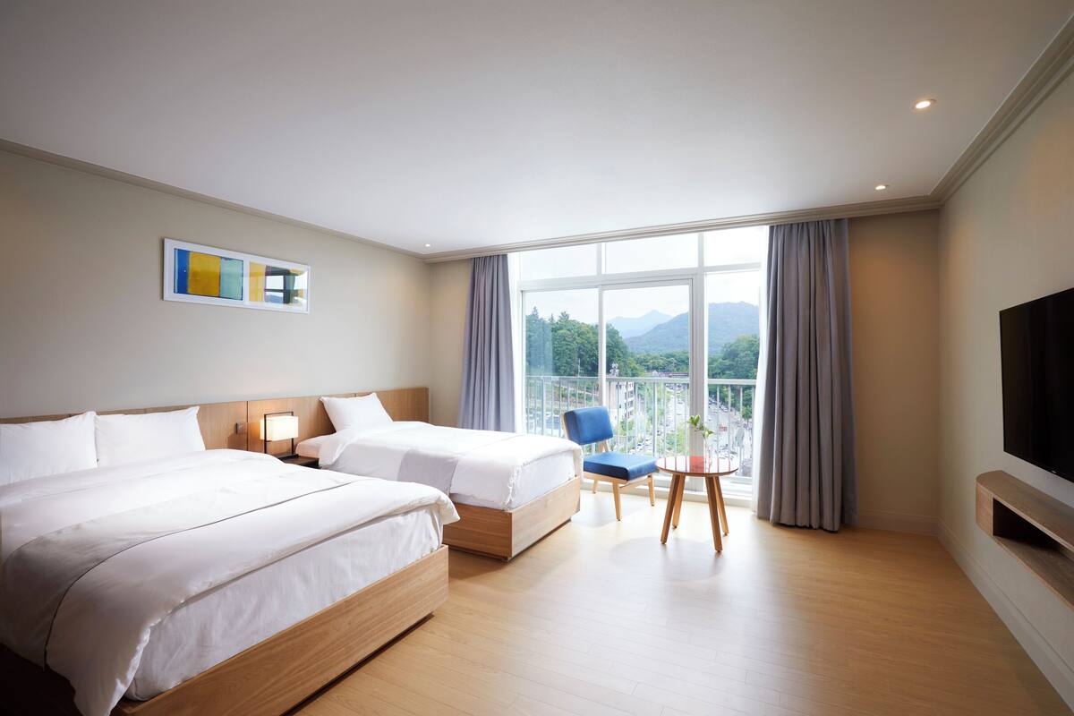 Une chambre d’hôtel avec deux lits, une télévision, un balcon donnant sur les montagnes et une petite table avec une chaise.