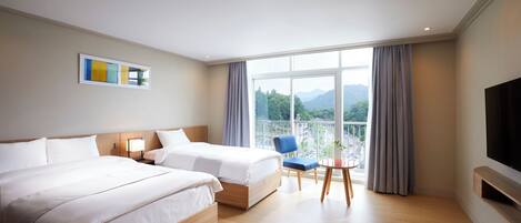 A hotel room with two beds, a TV, a balcony with a view of mountains, and a small table with a chair.