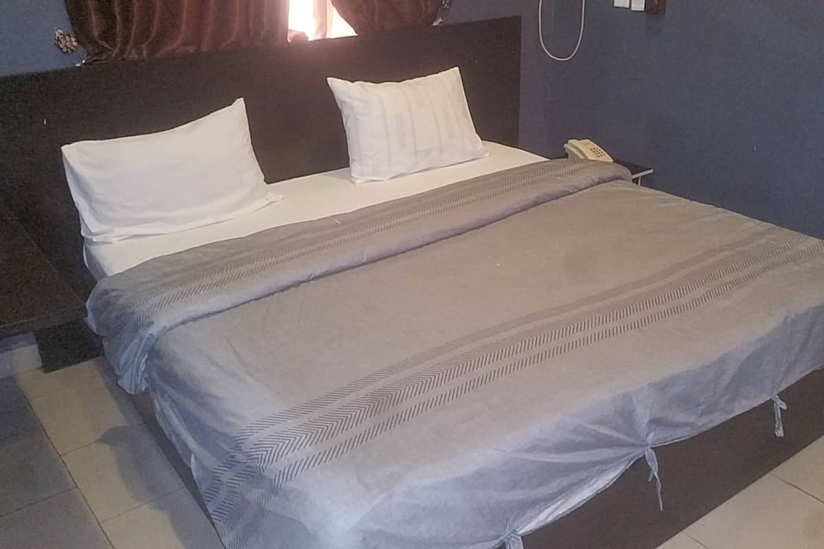 Ein ordentlich bezogenes Bett mit grauer Tagesdecke und weißen Kissen, einem Nachttischtelefon und einem braunen Kopfteil.