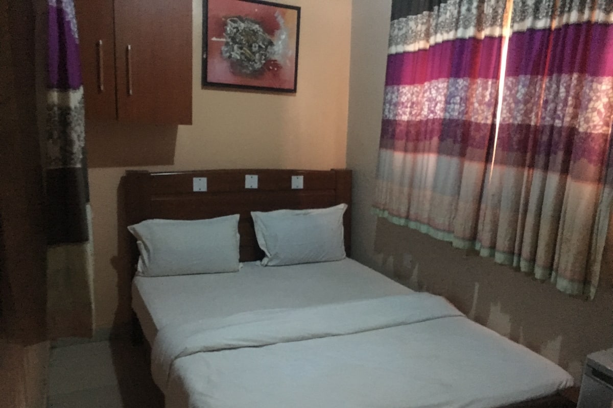 Ein Schlafzimmer mit Bett, Kissen, Kopfteil, Wandbild und einem Fenster mit Vorhängen.