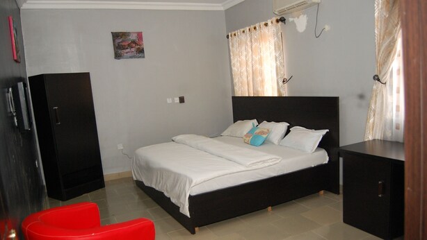 A bedroom with a bed, a red chair, a black wardrobe, and a small table.