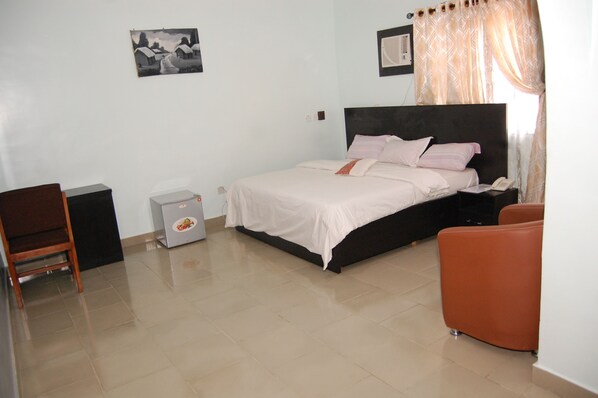 A bedroom with a bed, a chair, a small table, and a nightstand.