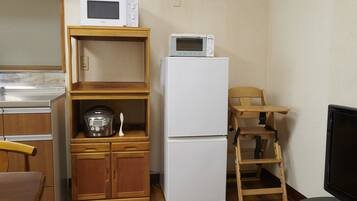 A compact kitchen with a microwave, a refrigerator, a wooden cabinet, a chair, and a television.
