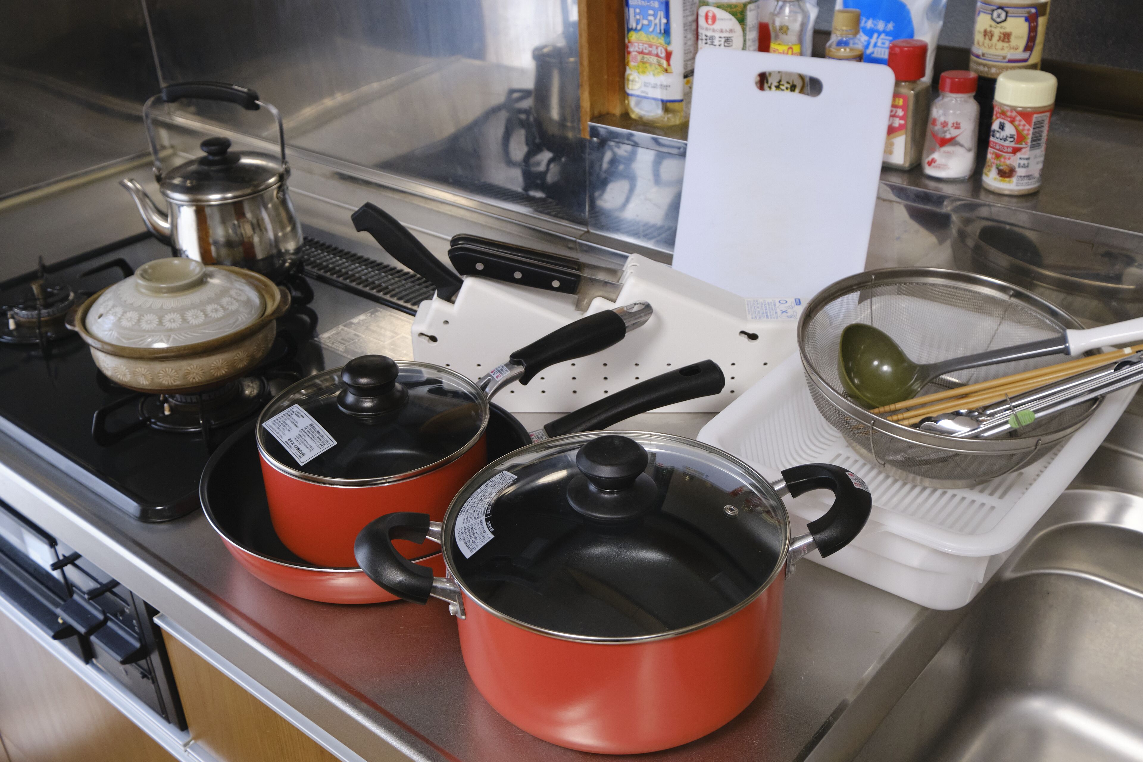 A kitchen with two red pots on the stove, a kettle, a cutting board, and various kitchen utensils.