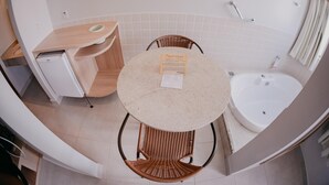 Un baño pequeño con una mesa redonda, sillas de mimbre, una bañera blanca y un mueble pequeño.