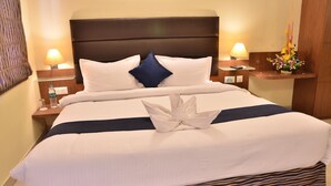 A neatly made bed with white linens, a dark headboard, and a decorative flower arrangement on the nightstand. - LBD Resorts & Hotels (Kolkata)