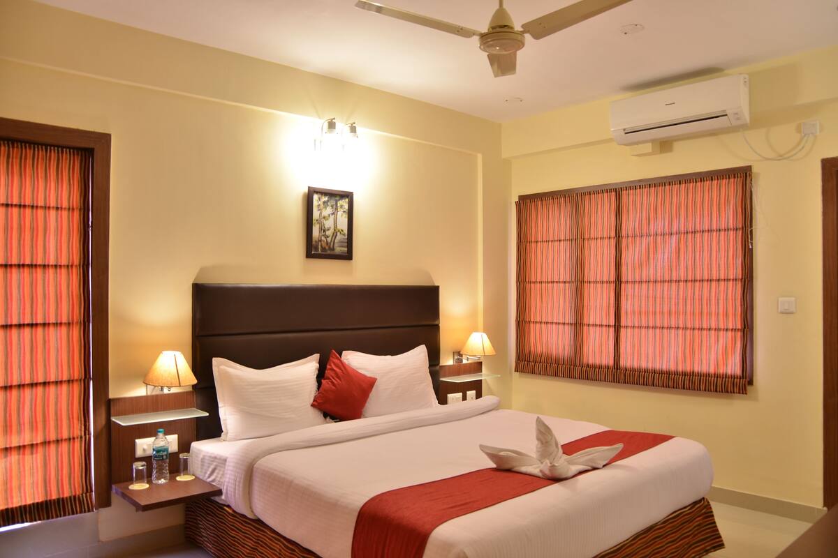 Une chambre d’hôtel comprenant un lit, deux tables de chevet, un ventilateur de plafond, un appareil de climatisation et des rideaux.
