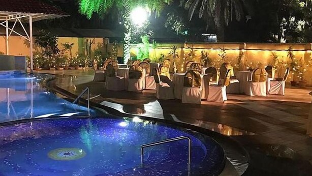 An outdoor pool area with seating around the perimeter, a covered area with a roof, and a well-lit walkway. - LBD Resorts & Hotels (Kolkata)