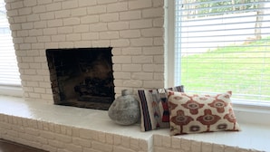 Una chimenea con paredes de ladrillo blanco, una maceta de piedra y cojines estampados en un banco.