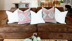 Una sala de estar acogedora con un sofá marrón, cojines estampados y una mesita de centro con suculentas.