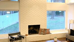 Una sala de estar con chimenea de ladrillo blanco, una butaca negra, una mesa de centro de madera y un sofá.