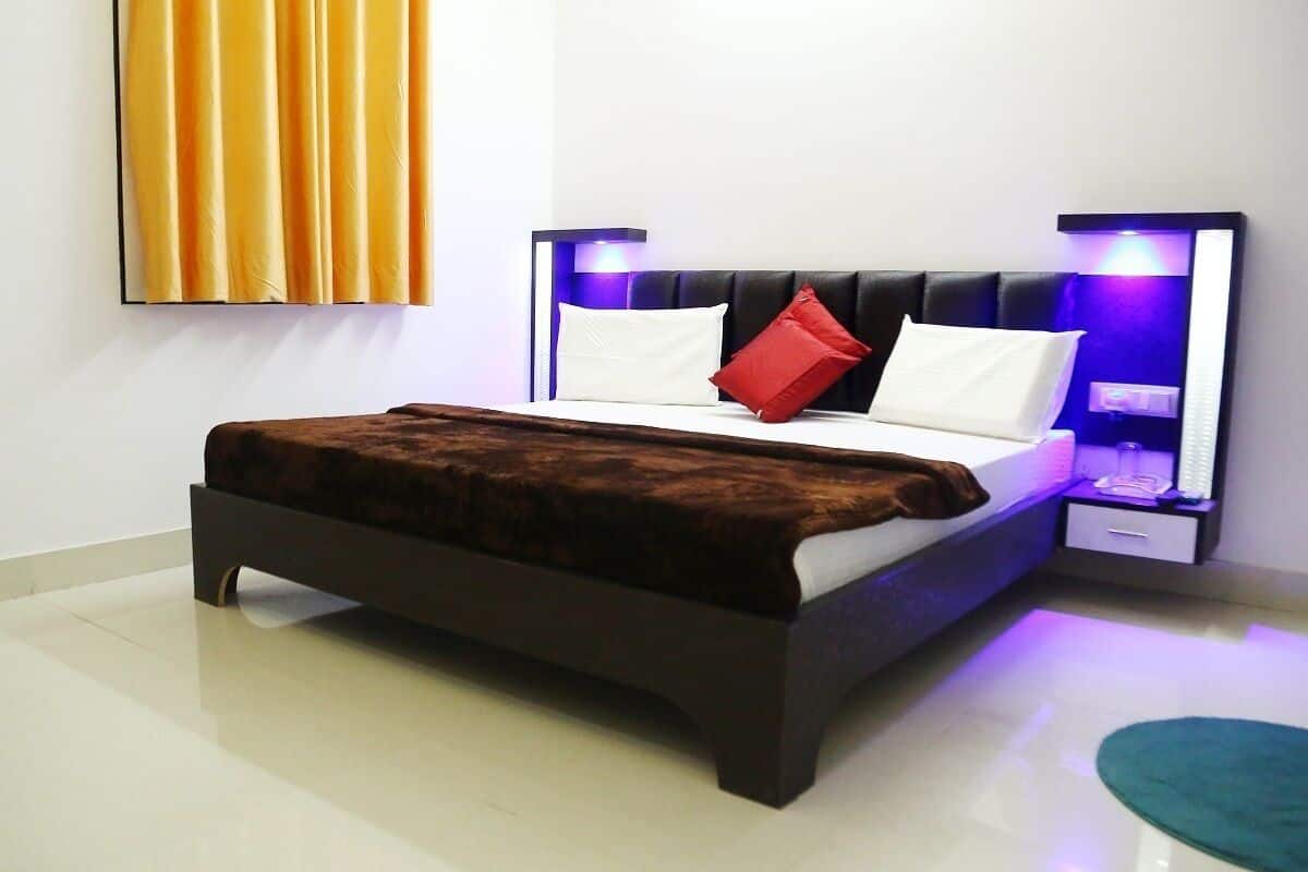 A modern bedroom with a dark wooden bed, white and red pillows, and two bedside tables with blue lighting.