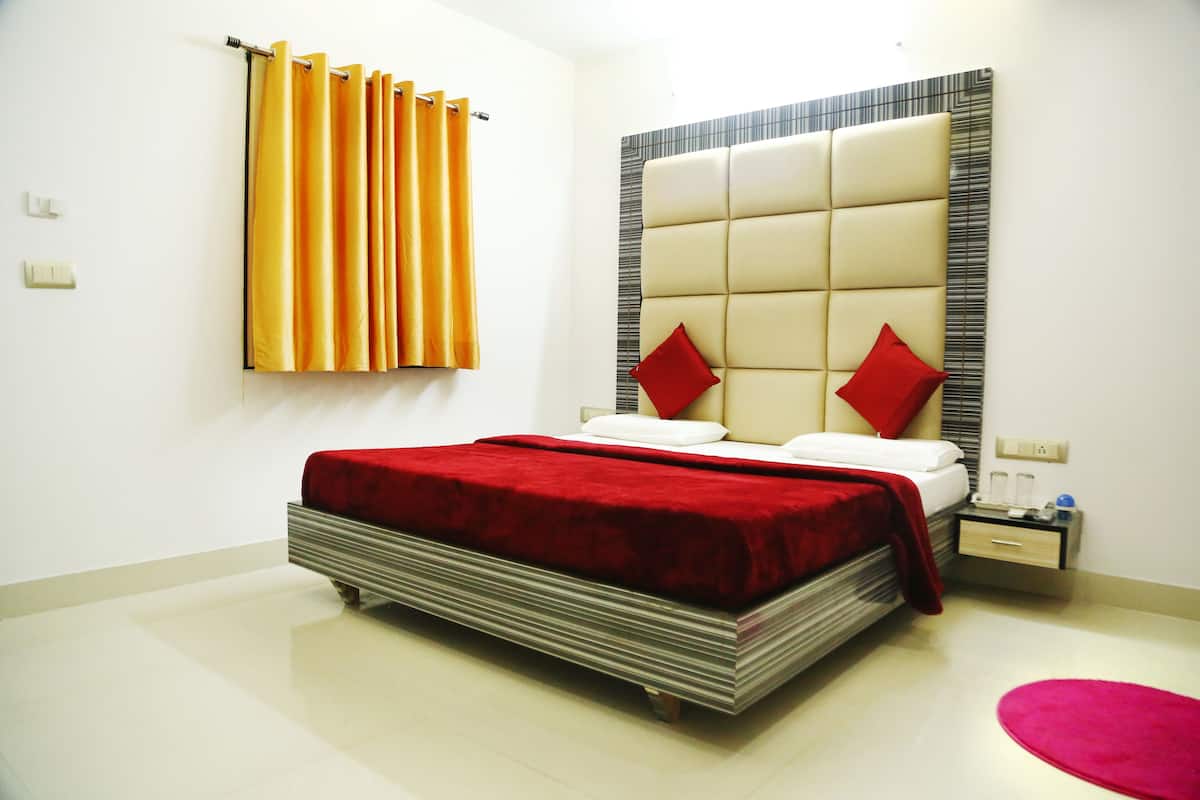 A hotel room with a bed, a nightstand, a red rug, and a window with curtains.