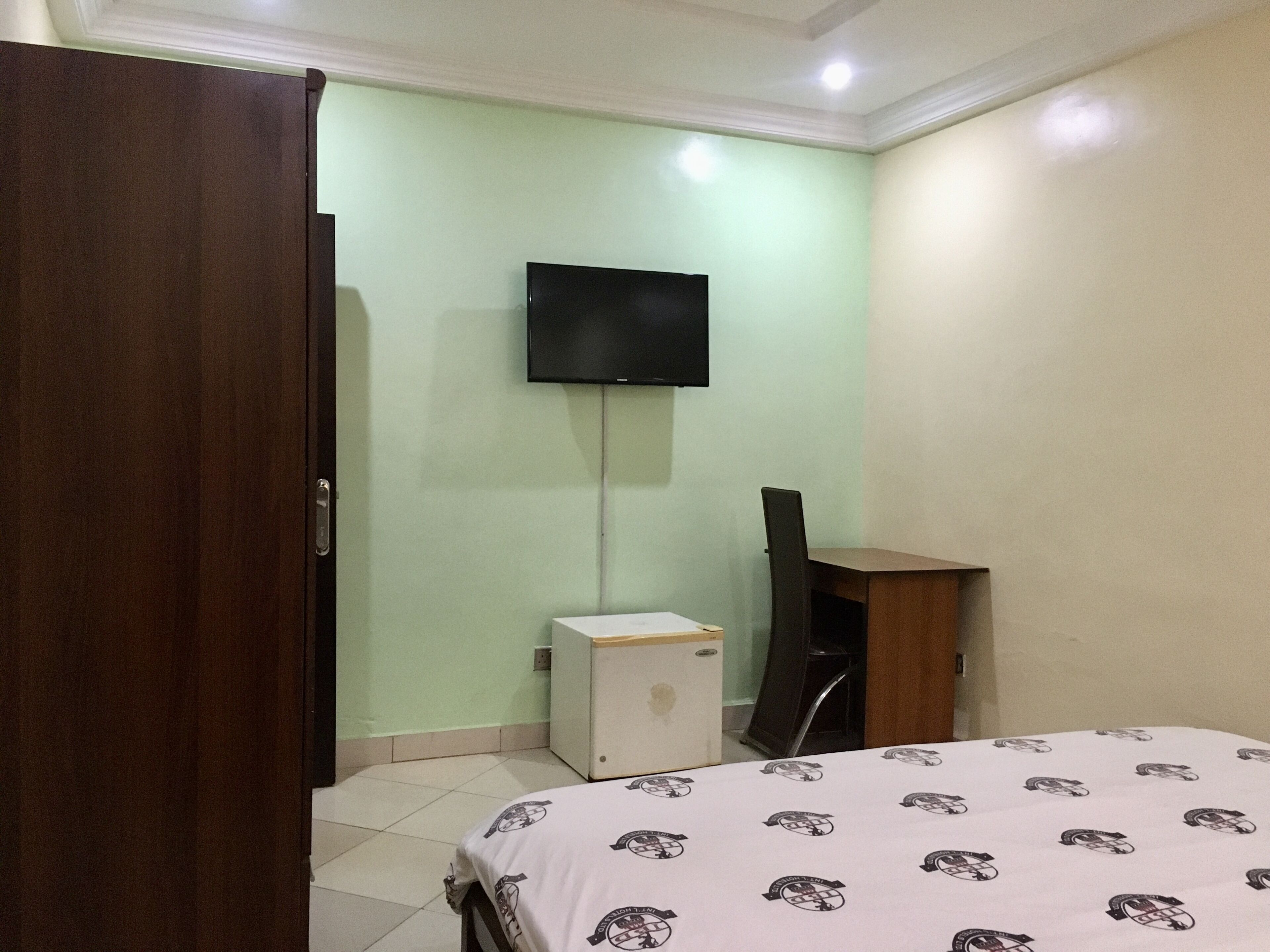 A bedroom with a bed, a TV mounted on the wall, a small white cabinet, and a wooden cabinet.