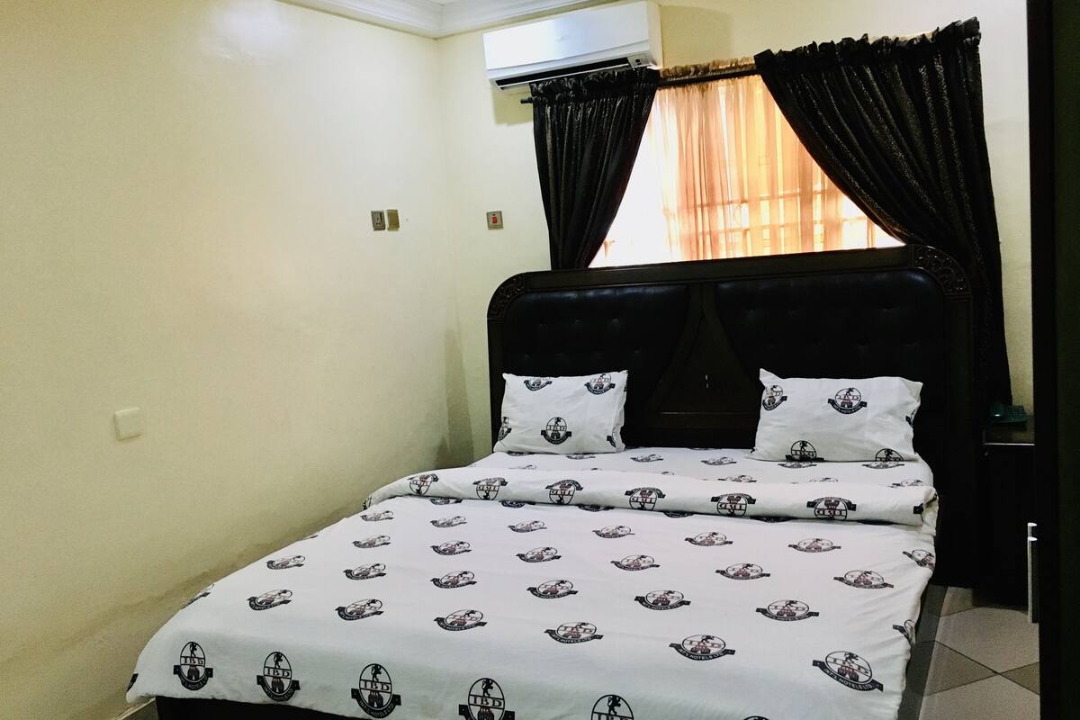 A bed with a patterned bedspread, a dark headboard, and black curtains.