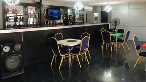 A bar area with a counter, multiple bottles of alcohol, a television, and a seating area with chairs and a table. - IBD International Hotel Ilaro (Ilaro)