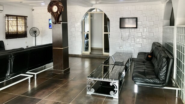 A modern lobby with a reception desk, a black leather sofa, a glass coffee table, and a decorative clock. - IBD International Hotel Ilaro (Ilaro)