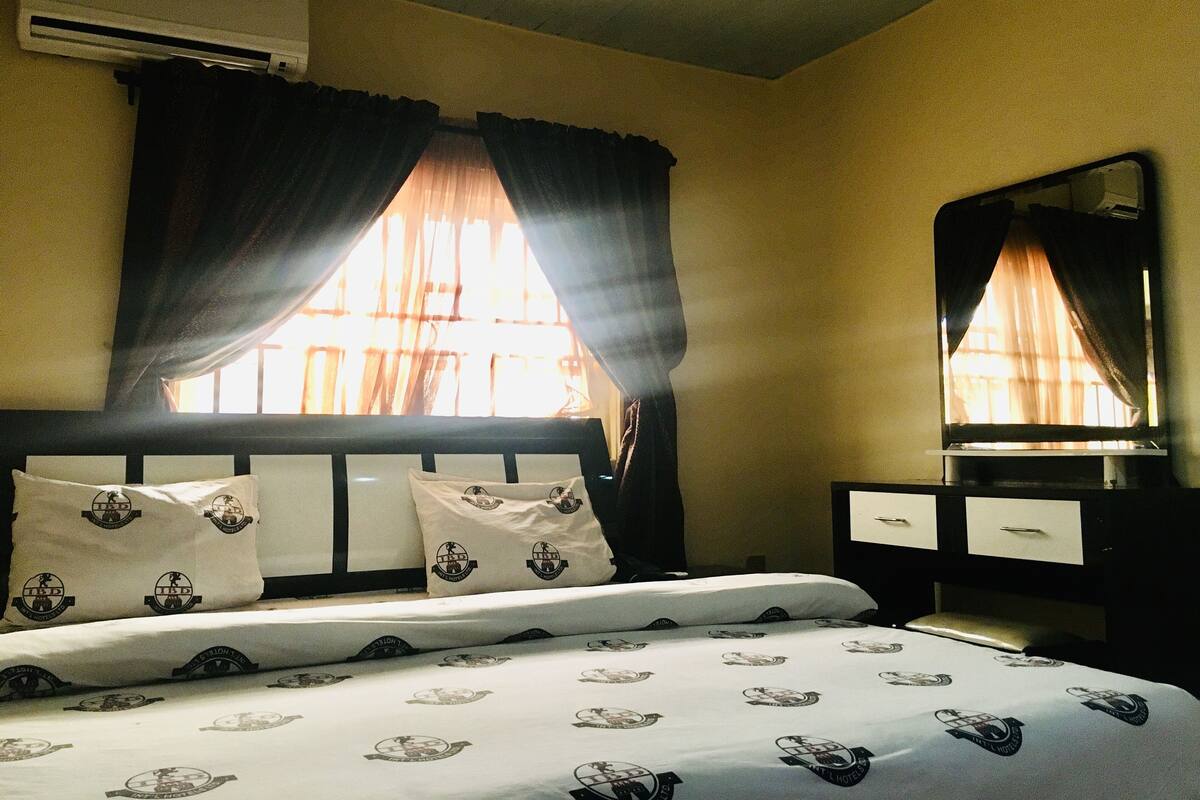 A hotel room with a bed, a nightstand, a mirror, and an air conditioning unit.