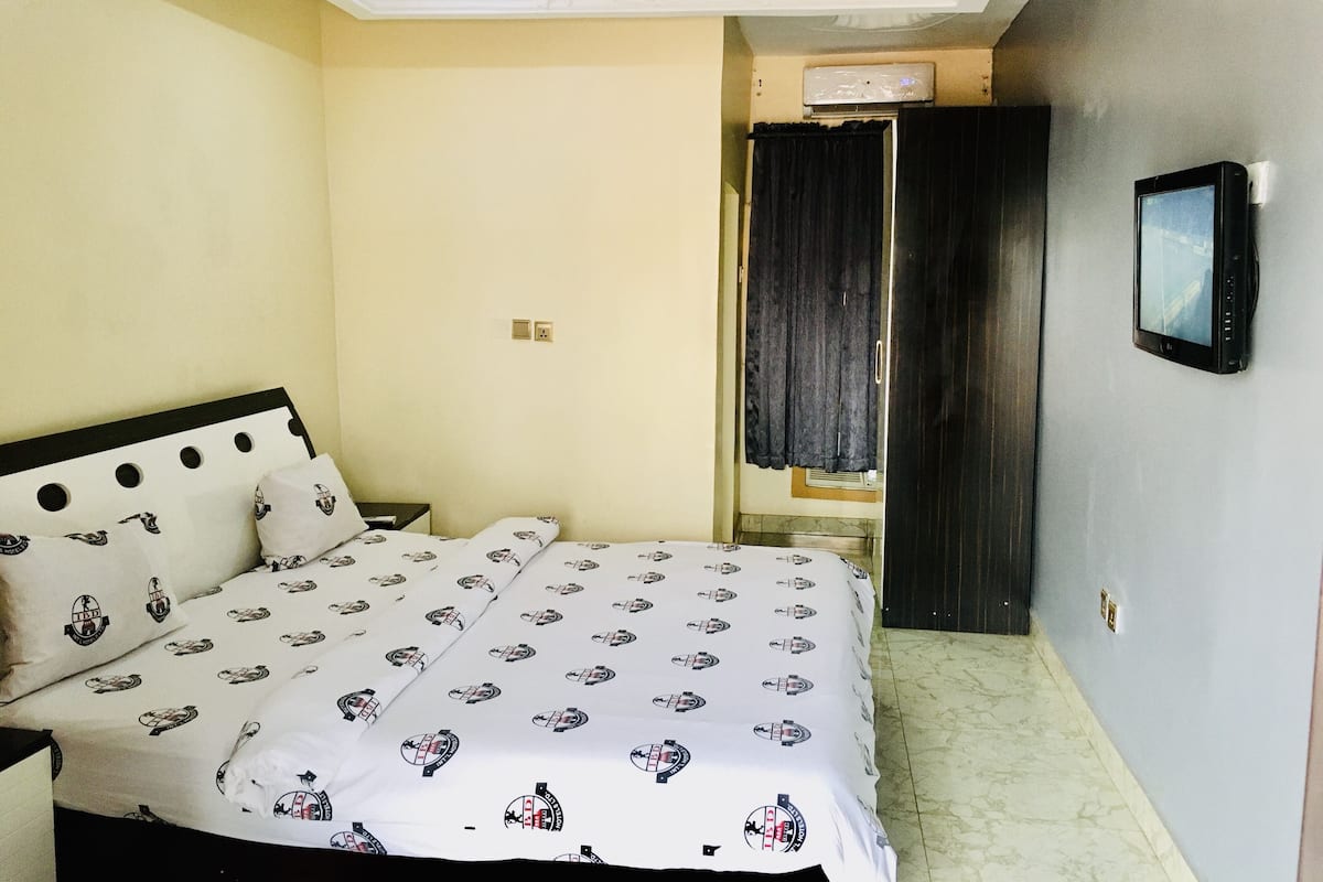 A bedroom with a bed, a TV mounted on the wall, and a door leading to another room.