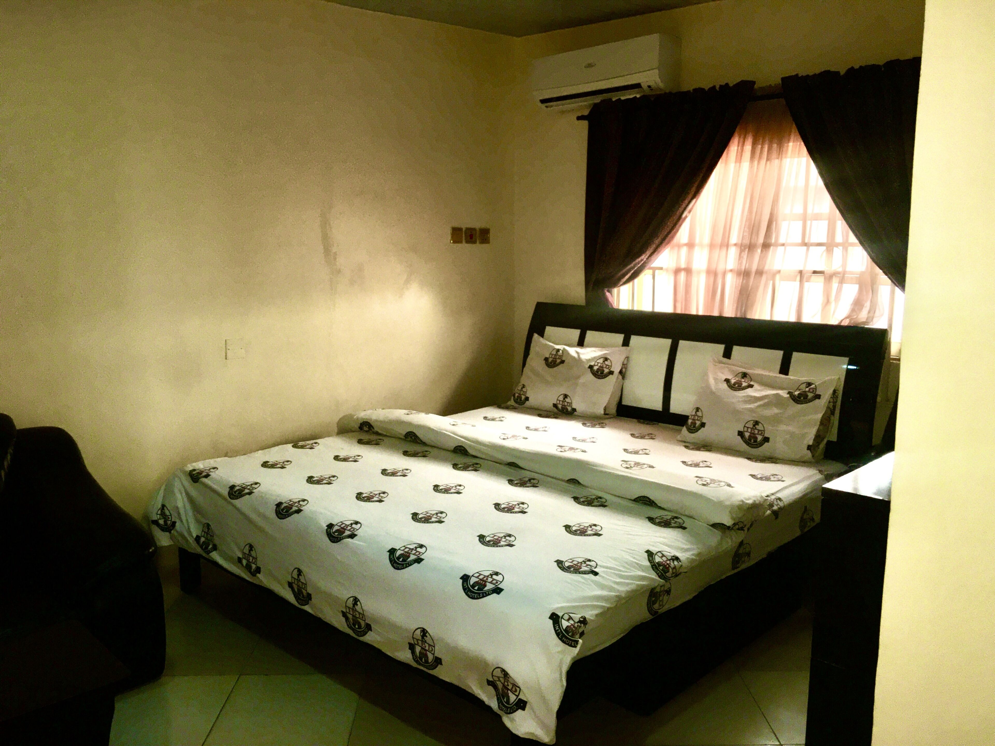 Una habitación pequeña y sencilla con cama, una silla y un equipo de aire acondicionado.
