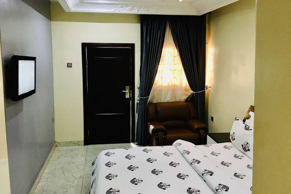 A hotel room with a bed, a chair, a television, and a door.