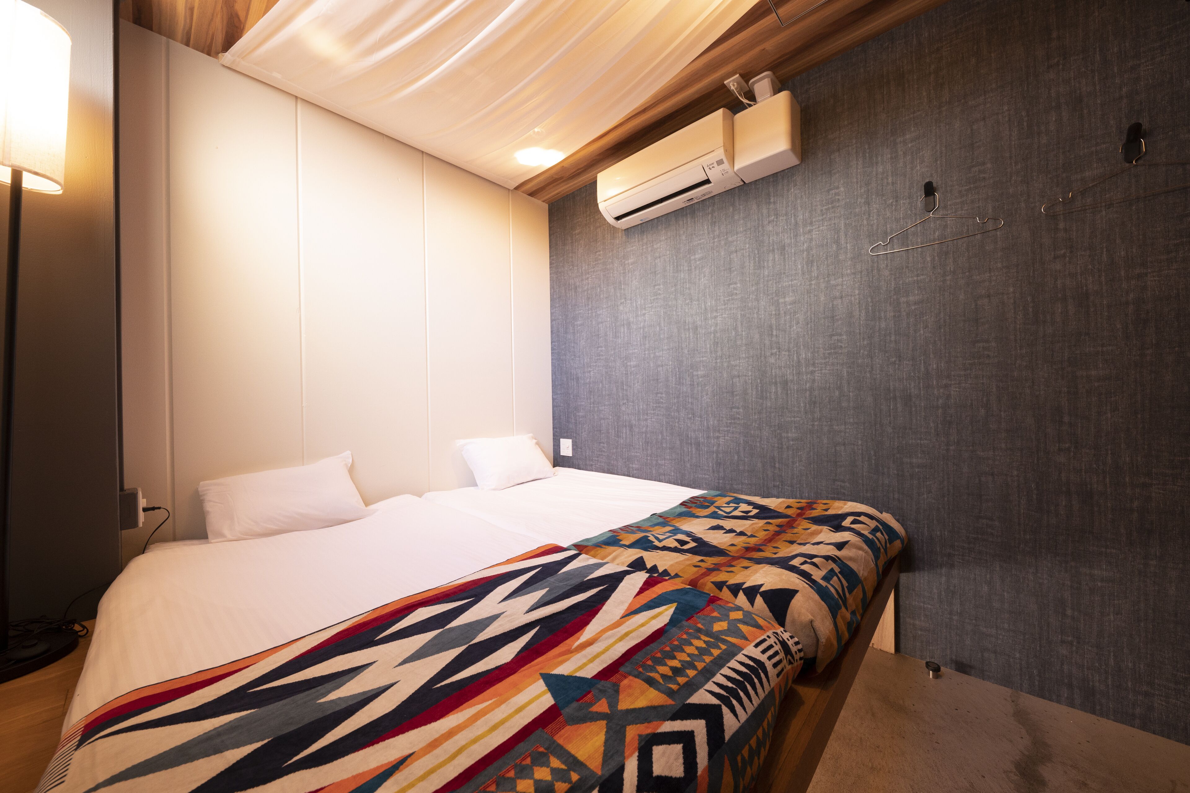 A hotel room with a bed, a wall-mounted air conditioner, and a hanging coat hook.