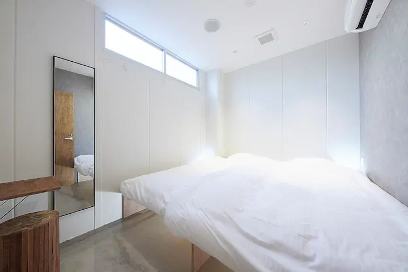 Ein modernes Schlafzimmer mit einem Bett, einem Holzhocker, einem Spiegel und einem Fenster.