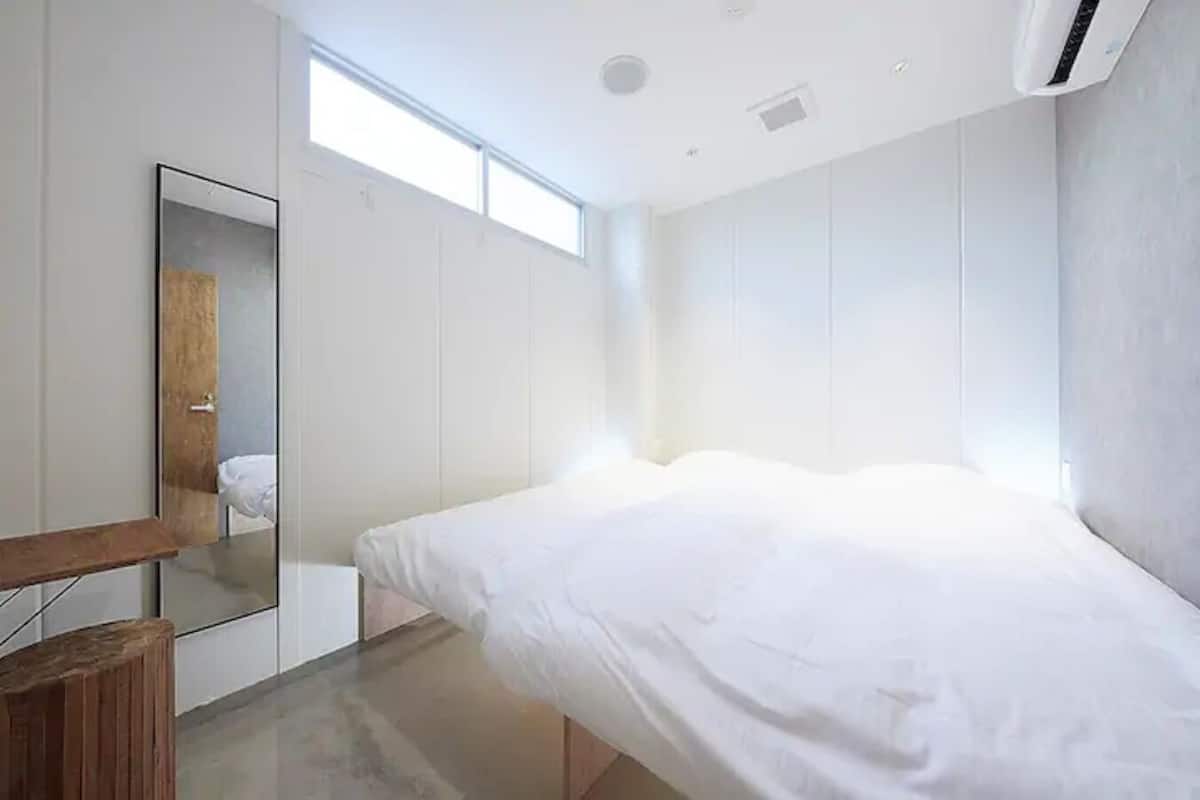 Une chambre à coucher moderne avec un lit, un tabouret en bois, un miroir et une fenêtre.