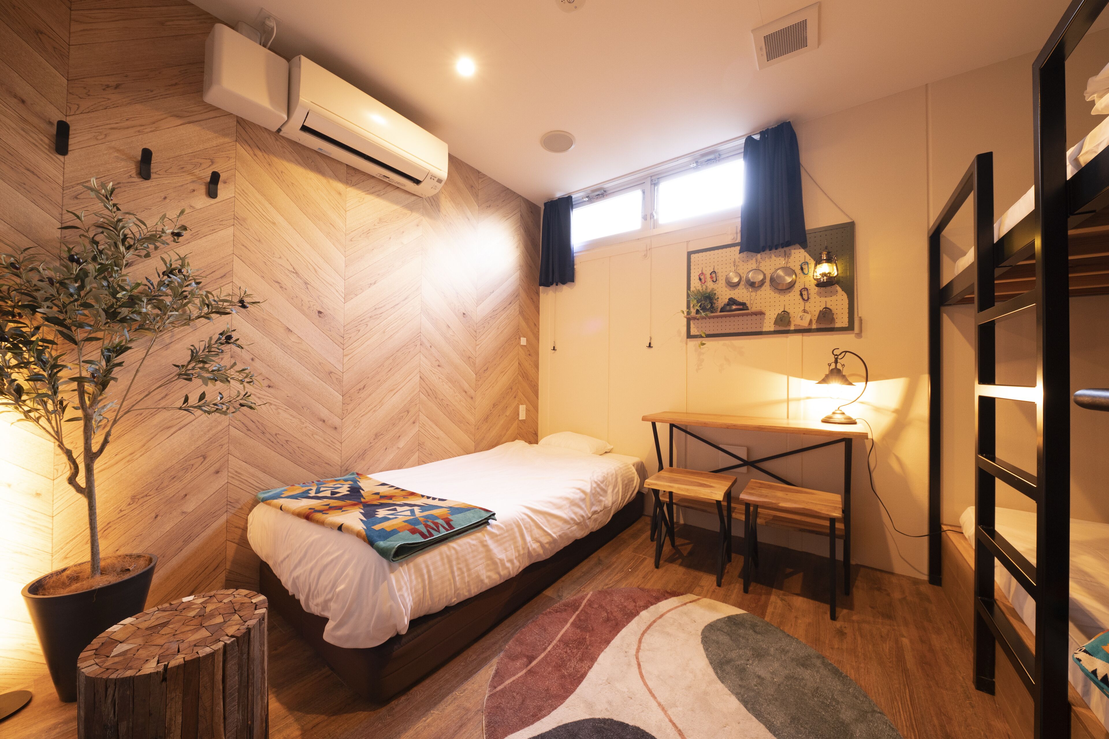 A compact bedroom with a bed, bedside table, desk, and a potted plant.
