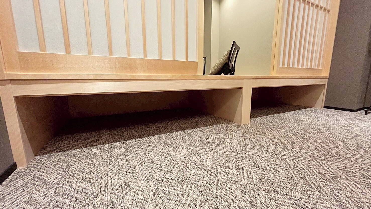 A carpeted room with a wooden bench, a mirror, and a door.