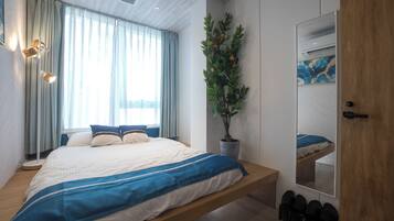 A bedroom with a bed, a bedside table, a mirror, a potted plant, and a shoe rack.
