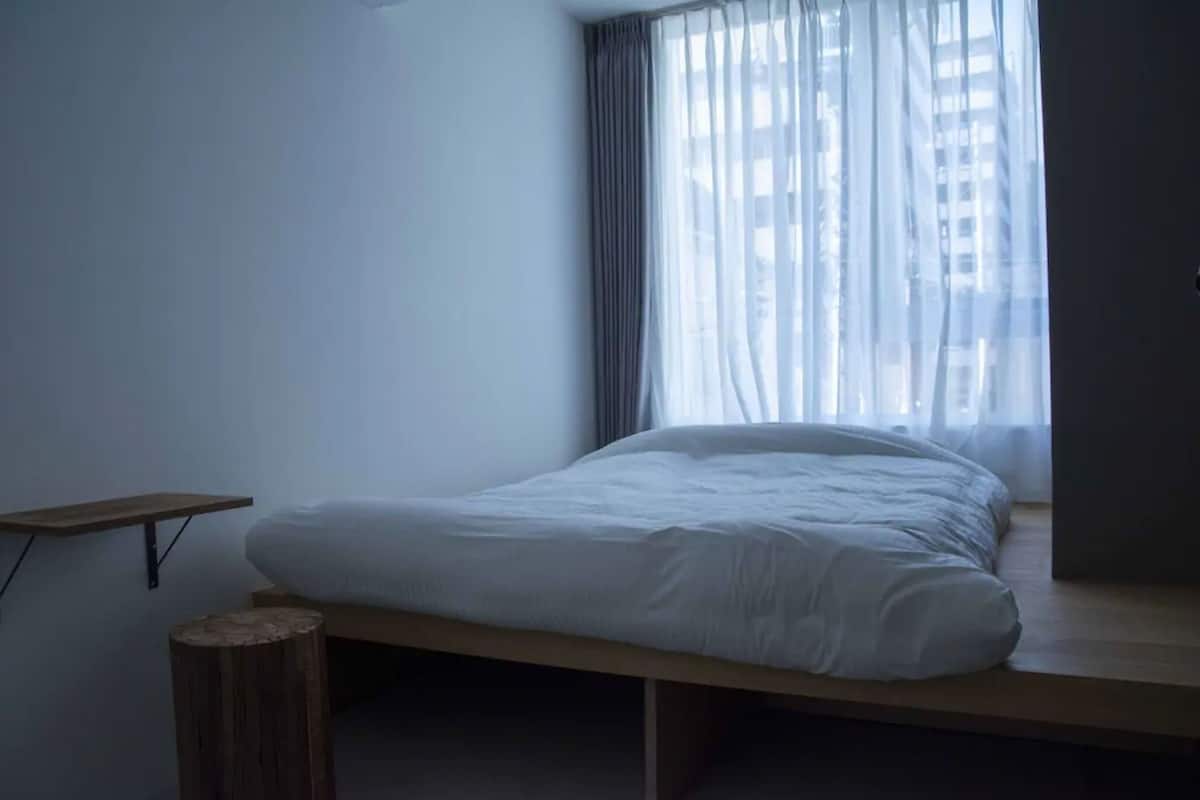 Une chambre à coucher minimaliste, avec un lit simple, un petit tabouret en bois et une étagère.