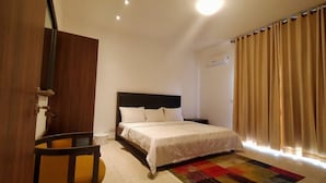 A hotel room with a bed, a chair, a small table, a colorful rug, and a window with curtains. - The Capital (Abuja)