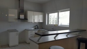 A modern kitchen with white cabinets, a stainless steel range hood, a window with a view, and a small refrigerator. - The Capital (Abuja)