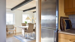 Moderni keittiö, jossa on ruostumattomasta teräksestä valmistettu jääkaappi, puukaapit sekä ruokailutila, jossa on pöytä ja tuolit.