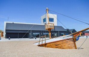 A wooden boat on a sandy beach with a modern building in the background.