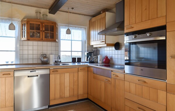 A kitchen with wooden cabinets, a stainless steel dishwasher, a built-in oven, and a window with a view of trees.
